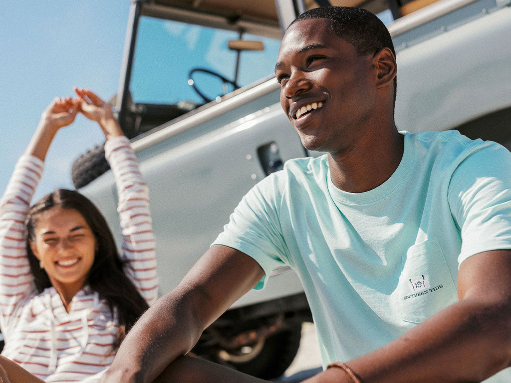 Man and woman siting beside car smiling.