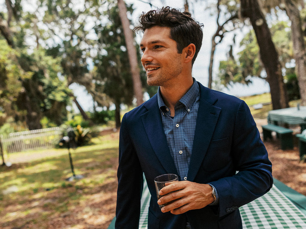 Man wearing a blazer and sport shirt outside holding a drink.