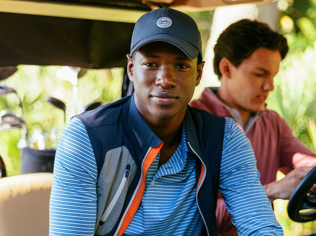 Man wearing hat, long sleeve shirt, and vest looking into camera.